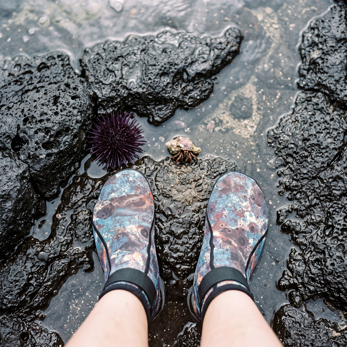 Looking down at a tide pool on volcanic rock while wearing the green camo Tilos 2mm Mid-High Top Socks with Velcro Straps