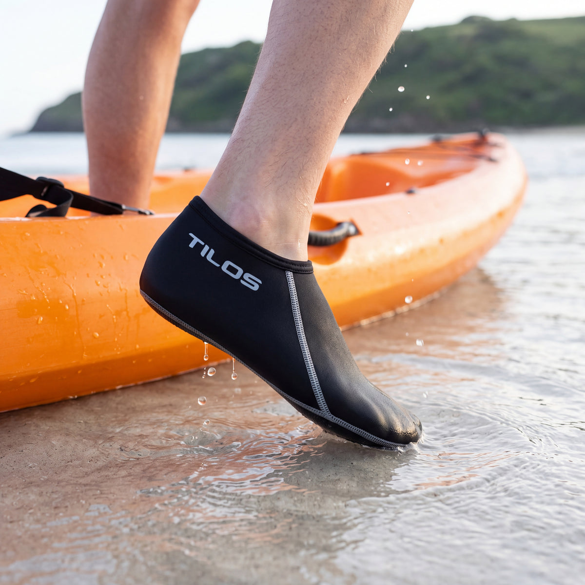 Kayaker stepping out of an orange kayak into clear shallows while wearing the black Tilos 3mm Short Neoprene Sock