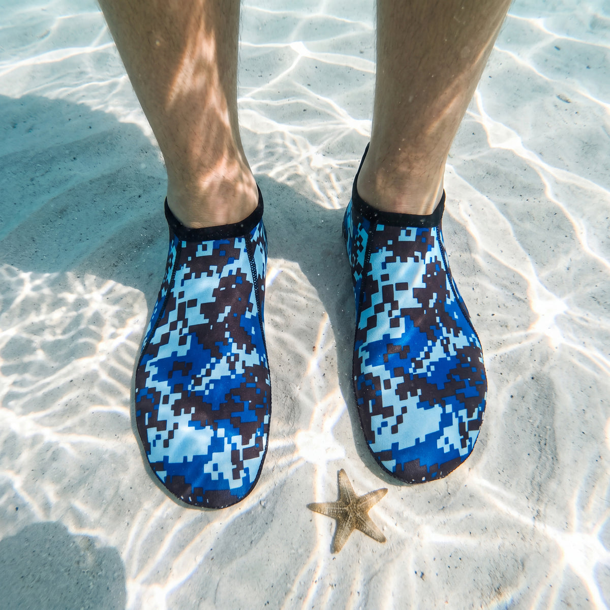 Looking down at your feet on a white sandbar in clear water while wearing the Digital Blue camo Tilos 3mm Short Neoprene Sock