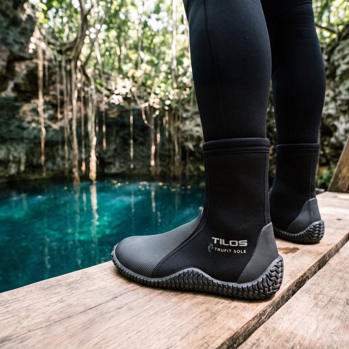Diver standing on a wooden platform beside a jungle cenote while wearing the black Tilos 5mm Thermoflare Semi-Dry Trufit Boot
