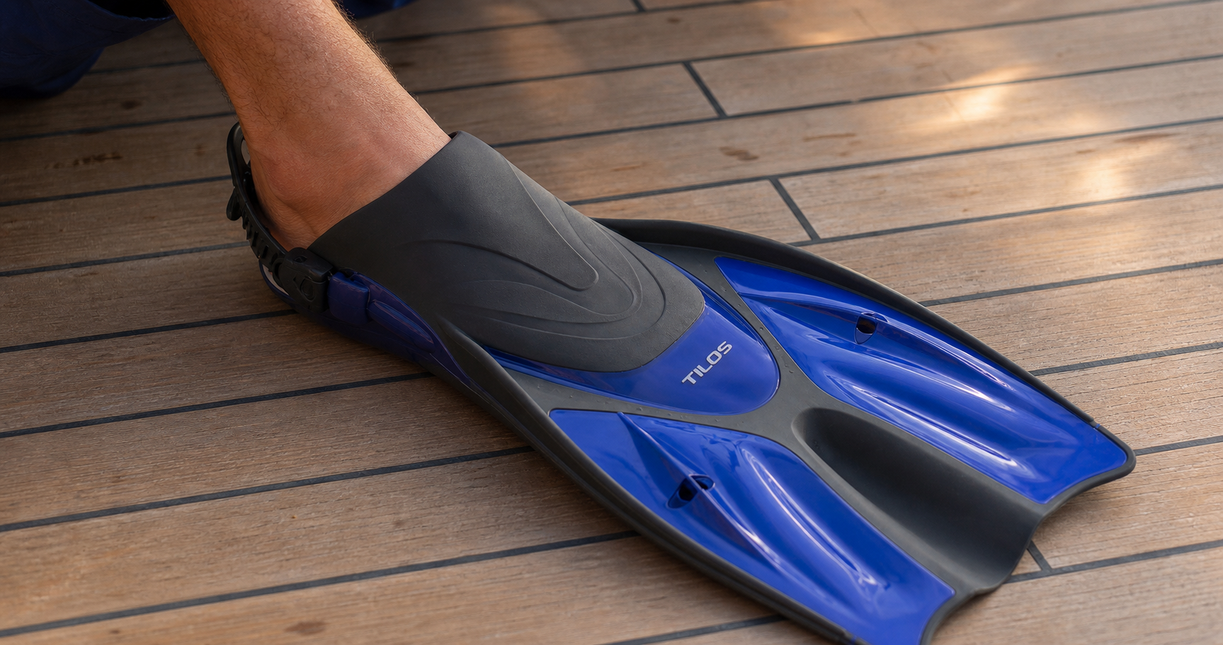 A foot settled into a blue Tilos Getaway open-heel fin on a boat deck, showing the wide toe box