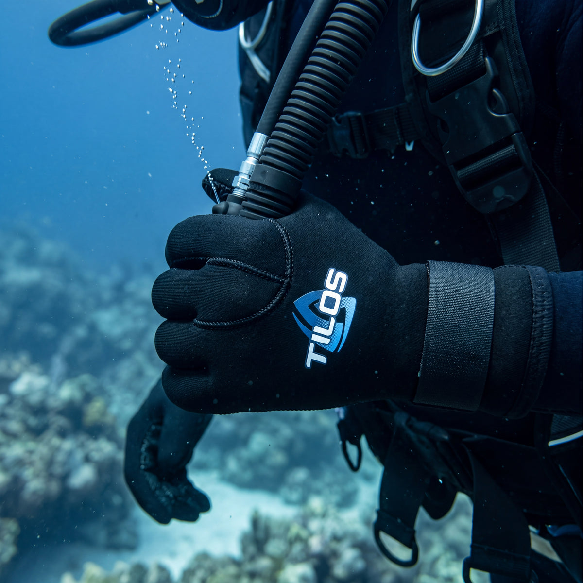 Diver underwater working a BCD inflator wearing a black Tilos 5mm Titanium neoprene glove, blue Tilos logo on the back of the hand.