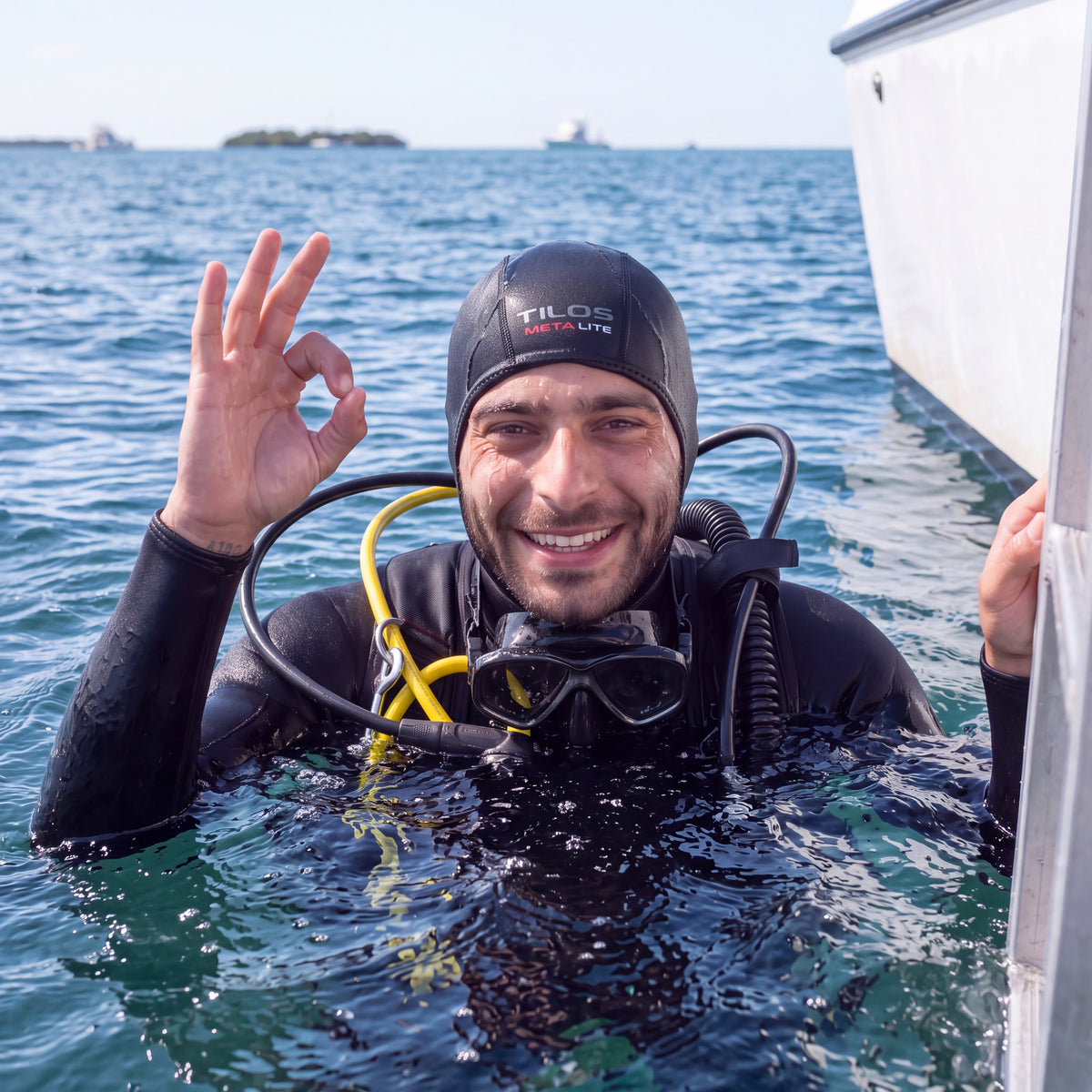 Diver at the surface in open water giving the OK signal to the boat, wearing a black Tilos 1mm titanium neoprene beanie.