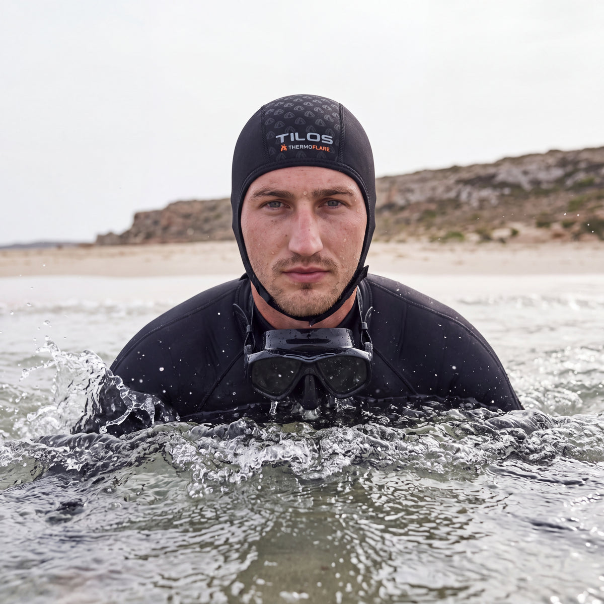 Snorkeler in the water pushing through the shore break wearing the Tilos 1mm Thermoflare Chin Strap Beanie in black