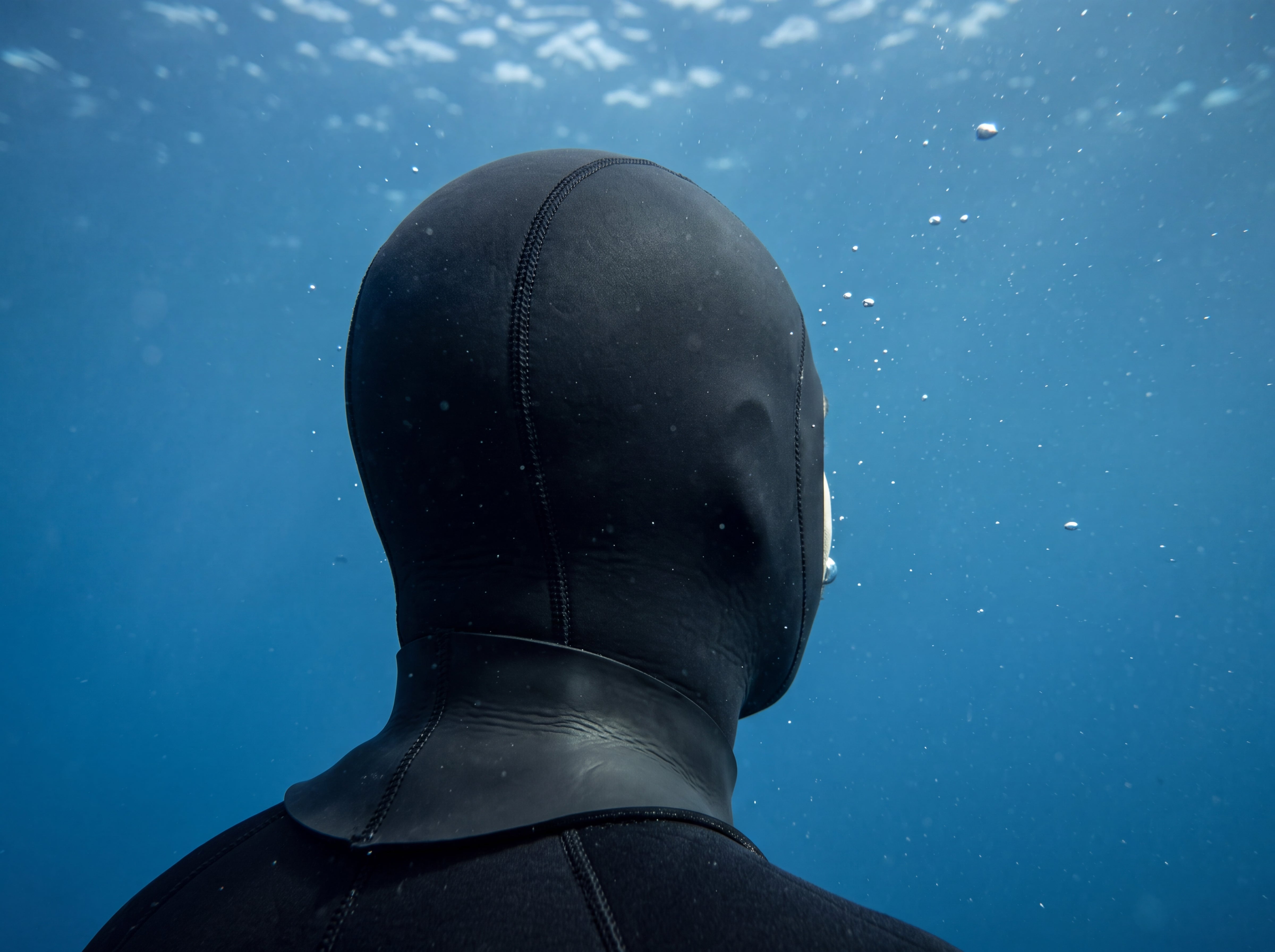 Freediver underwater wearing the Tilos 3mm Neoprene Dive Hood, rear three-quarter view showing the hood and glideskin neck seal