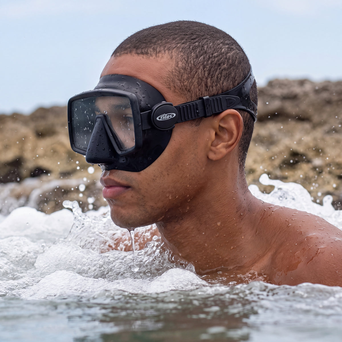 Snorkeler wading out through the shore break wearing the black Tilos Insight Frameless Mask