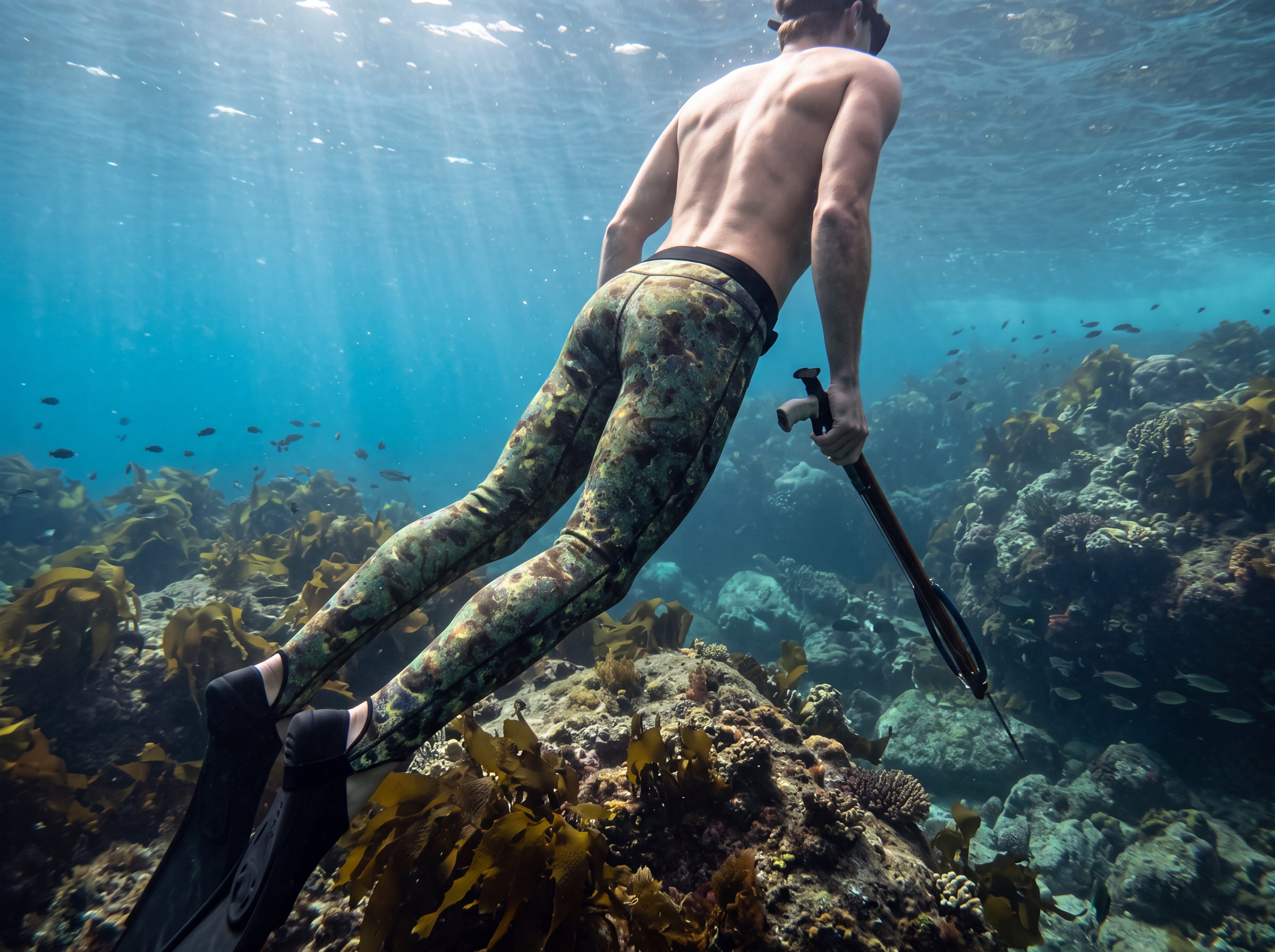Freediver in Tilos green reef-camo Spearfishing Pants descending along a coral reef with a speargun