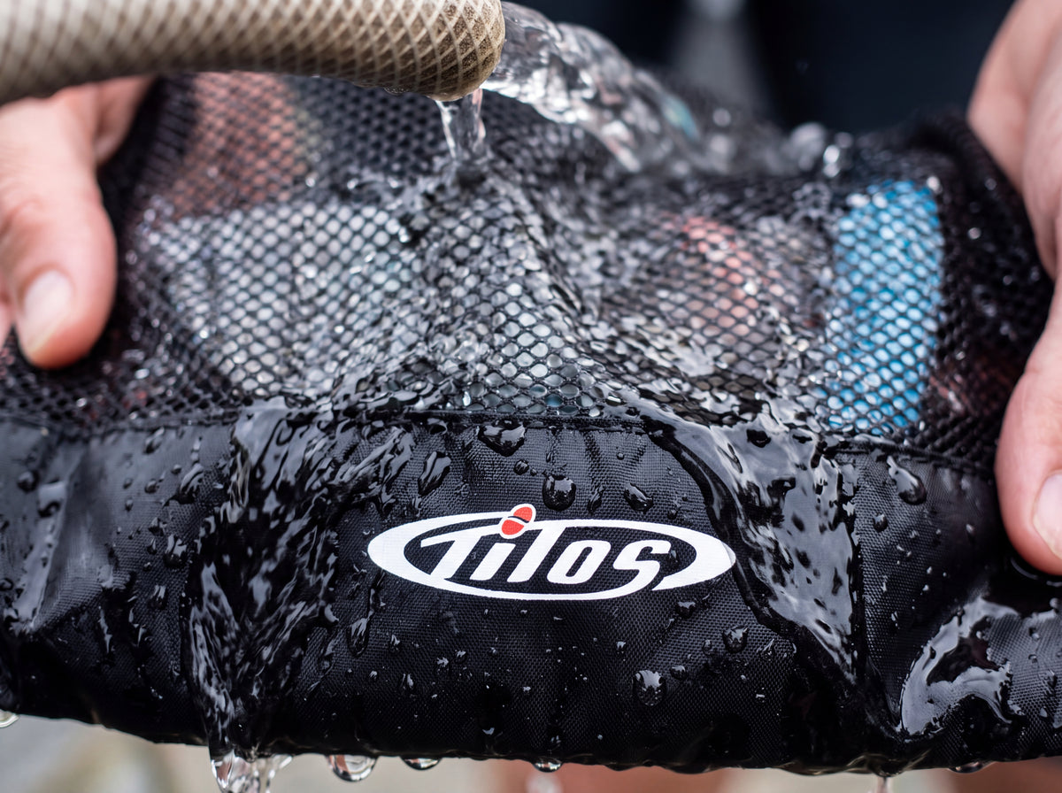 A diver rinses a black Tilos mesh mask and snorkel bag under fresh water after a dive.