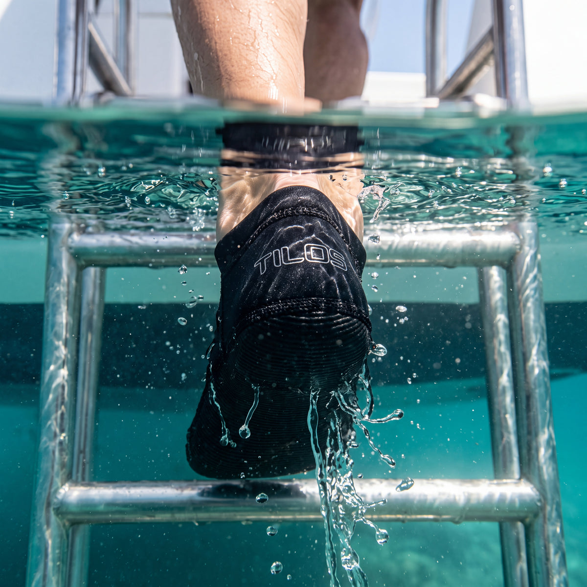 Snorkeler climbing a dive boat swim ladder wearing the black Tilos 2.5mm Low Cut Sport Skin Socks