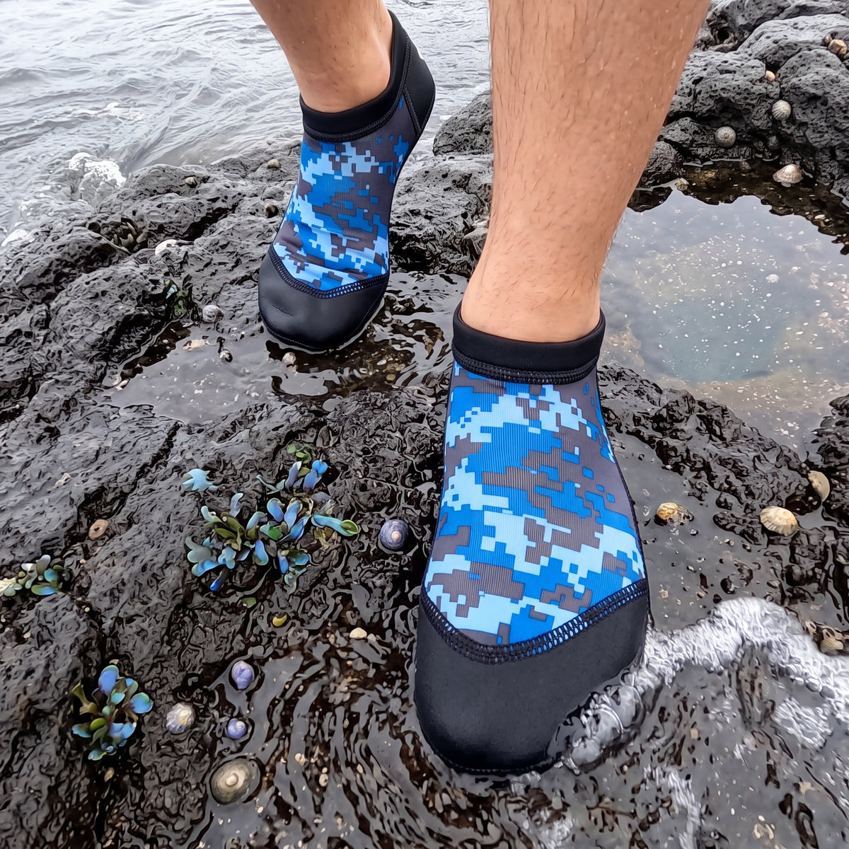 Tide pool explorer crossing wet volcanic rock wearing the digital blue camo Tilos 2.5mm Low Cut Sport Skin Socks