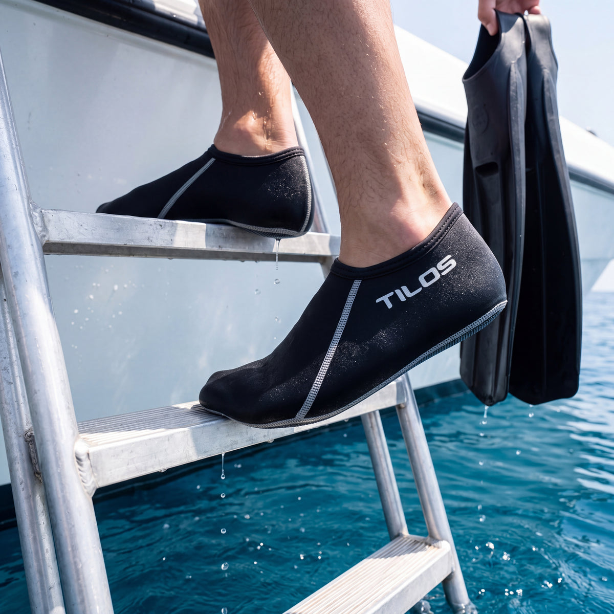 Diver climbing a dive boat ladder with fins in hand while wearing the black Tilos 3mm Short Neoprene Sock