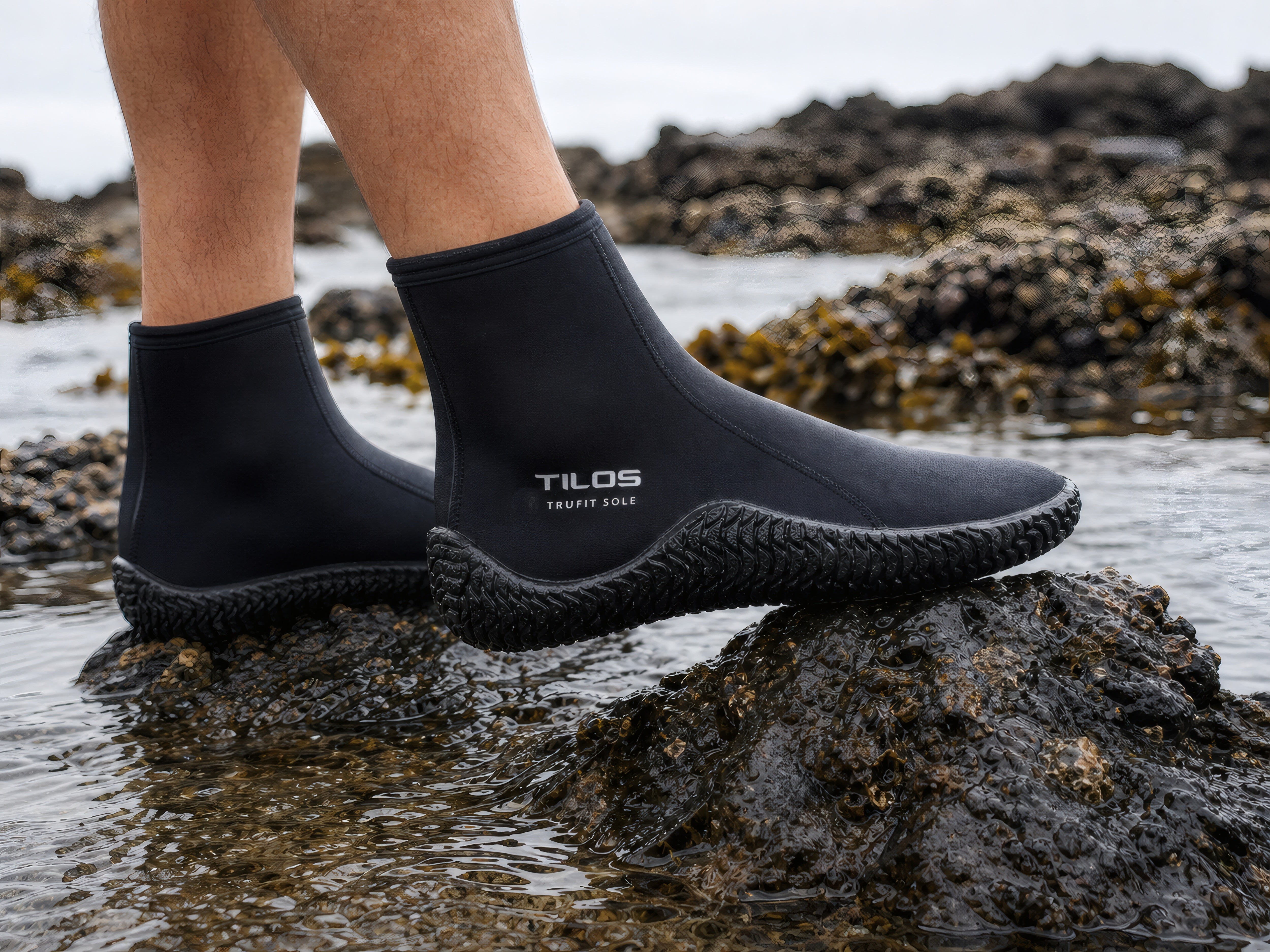 Diver wearing Tilos 3mm Titanium Zip Trufit Boots while stepping across a rocky tidepool with the TILOS TruFit Sole logo visible