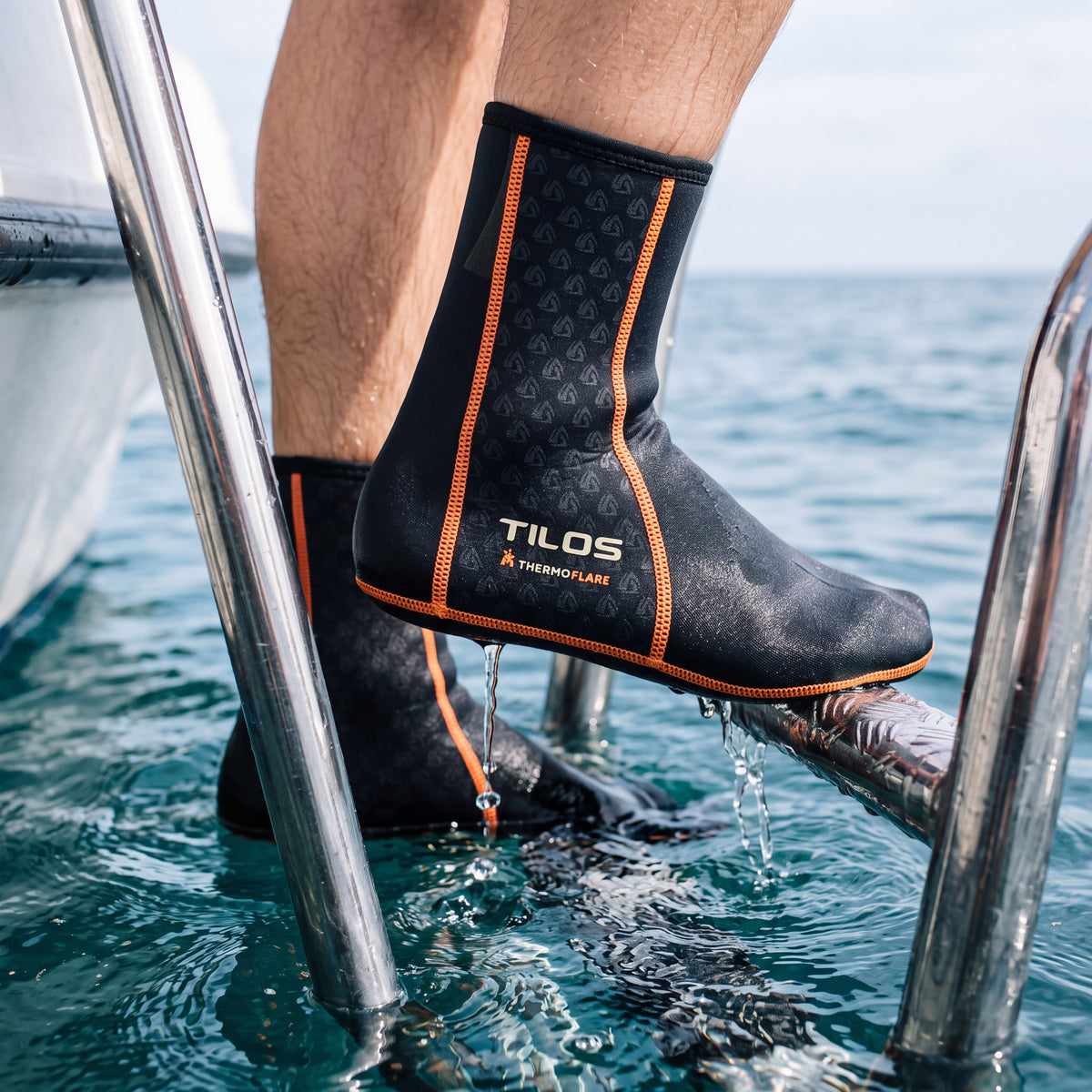 Snorkeler climbing a dive boat's stern ladder out of the sea while wearing the black Tilos 1mm Thermoflare Socks
