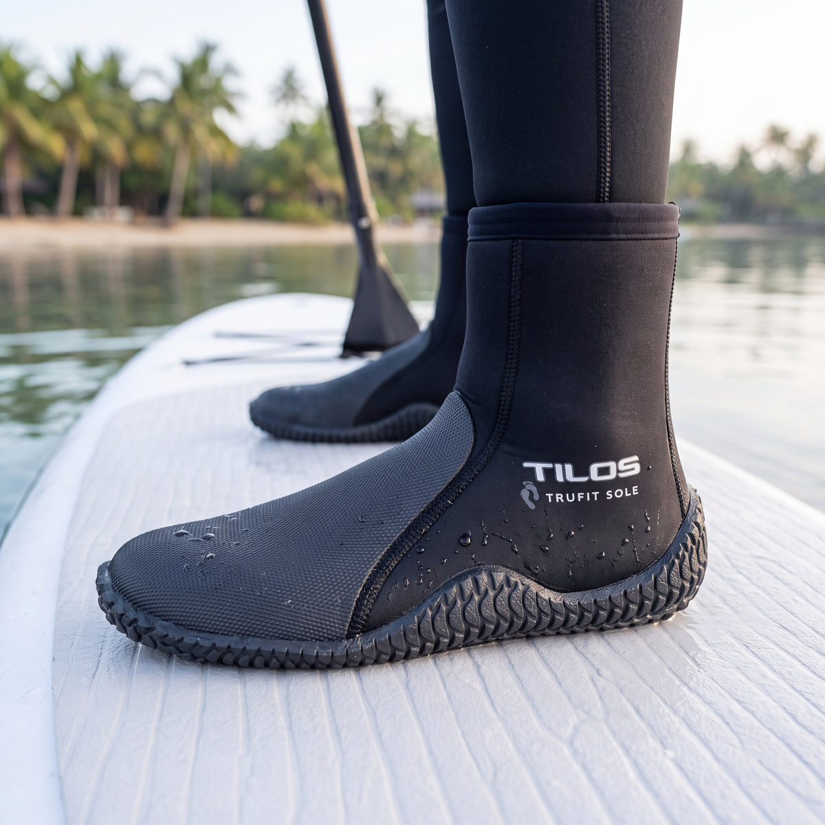 Paddleboarder standing on a white board in a calm lagoon while wearing the black Tilos 5mm Thermoflare Semi-Dry Trufit Boot