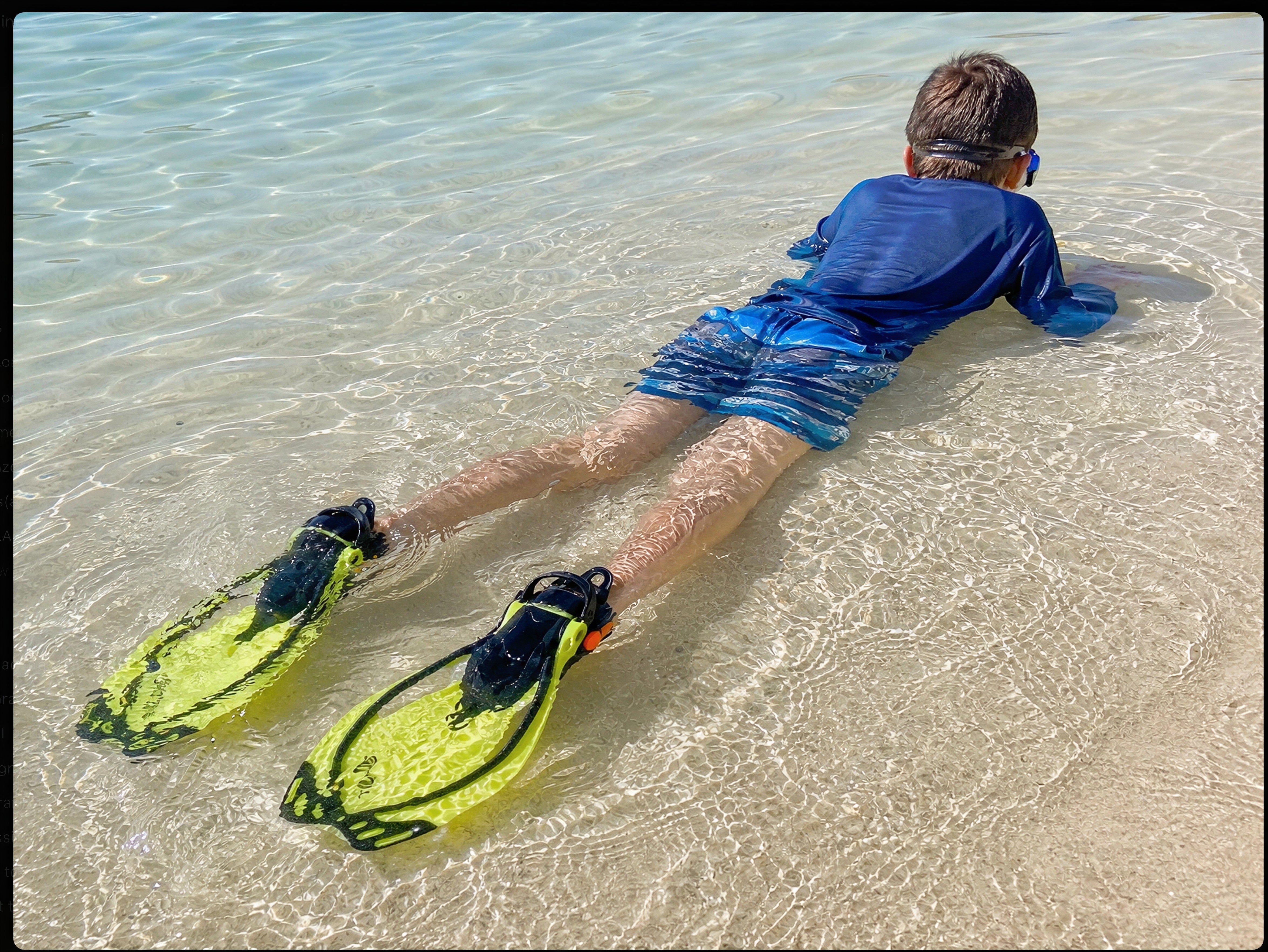 Lifestyle image of a child wearing yellow Tilos Vulcan Jr fins in shallow beach water