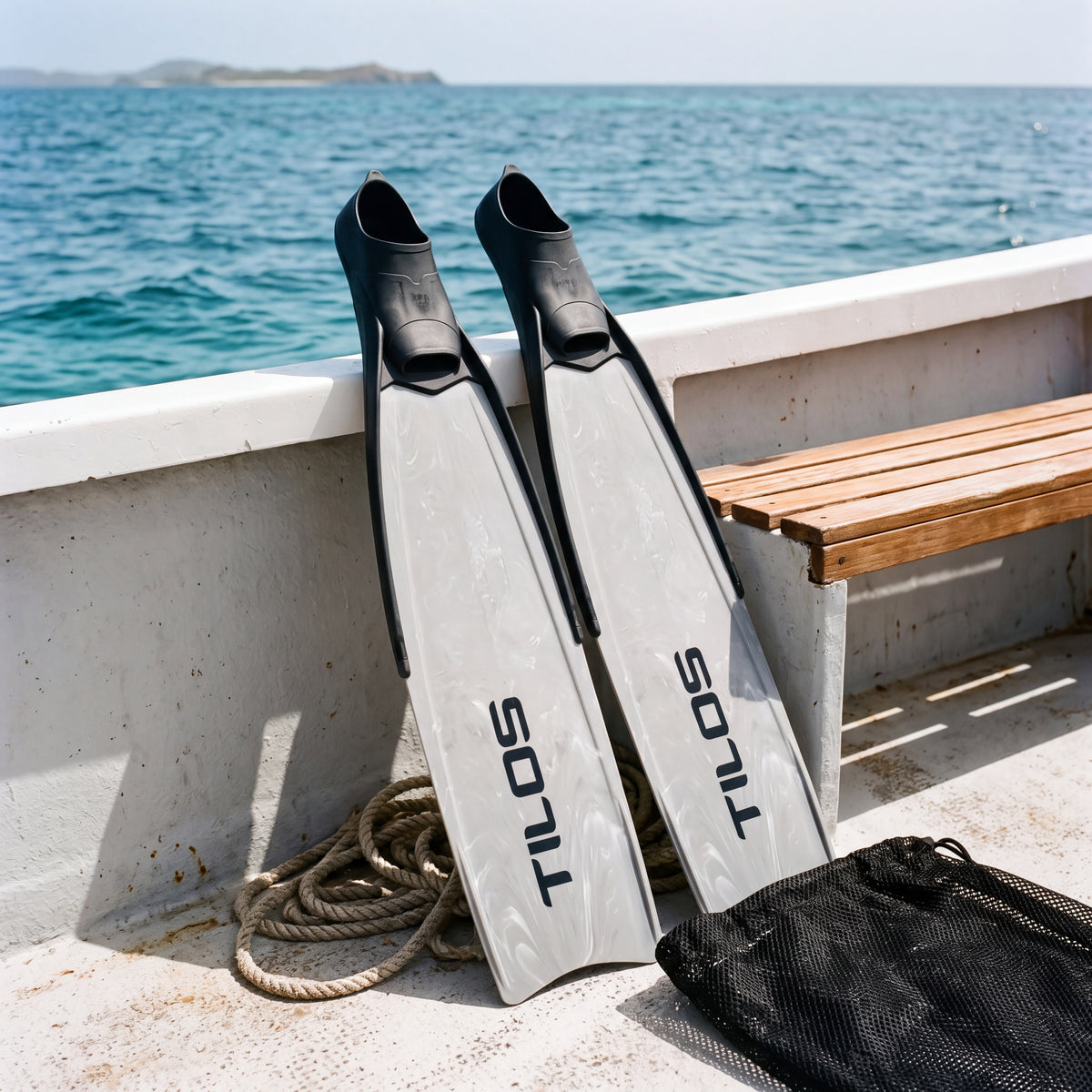 Lifestyle photo of a pair of Tilos Syryn full foot freediving fins in Black Camo leaning against the rail of a dive boat beside a teak bench