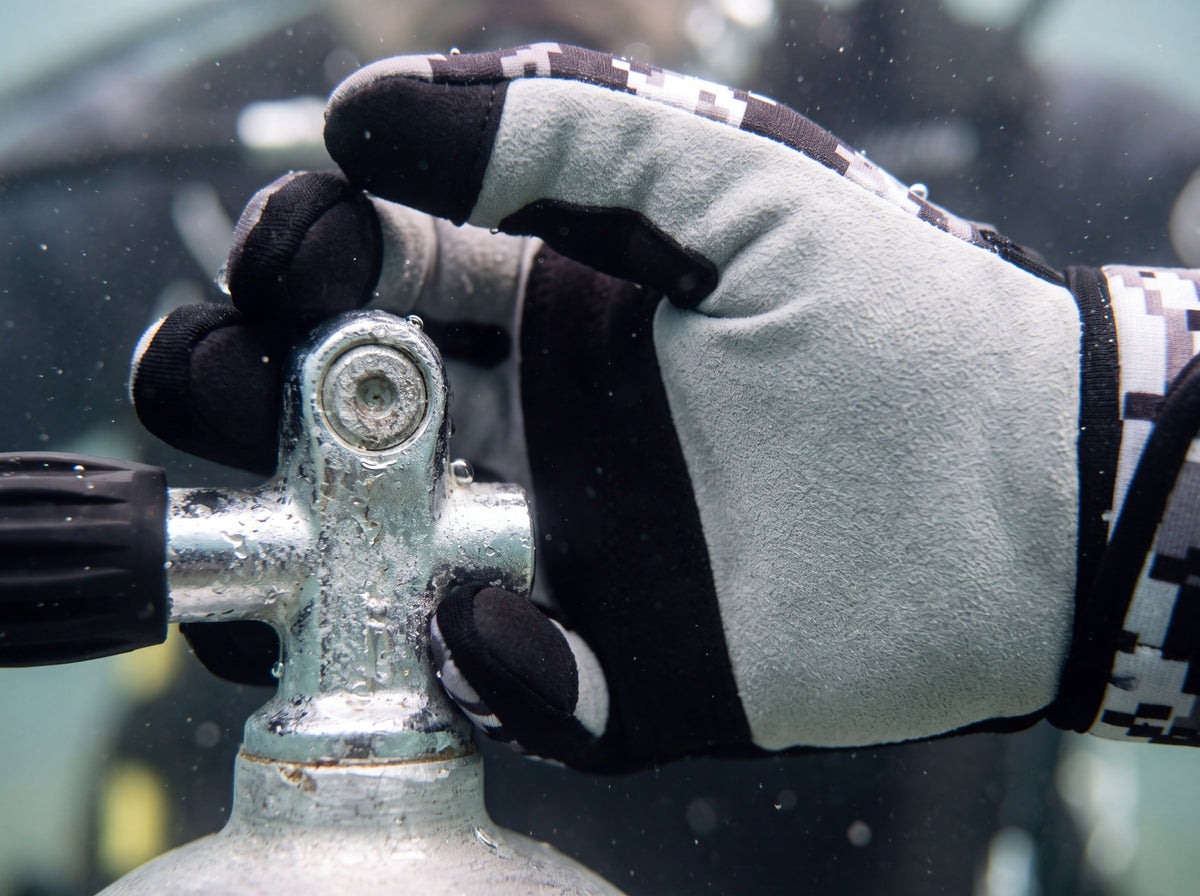 Close up of a diver's hand gripping a wet aluminium tank valve underwater, showing the light grey suede palm and black grip bands of a Digital Gray Tilos 1.5mm Tropical-X Mesh glove.