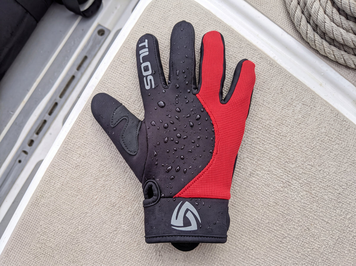 A diver's red accented Tilos 1.5mm Tropical-X Mesh glove rests on the wet non slip deck of a dive boat between dives, beaded with water and showing the wrist strap emblem.