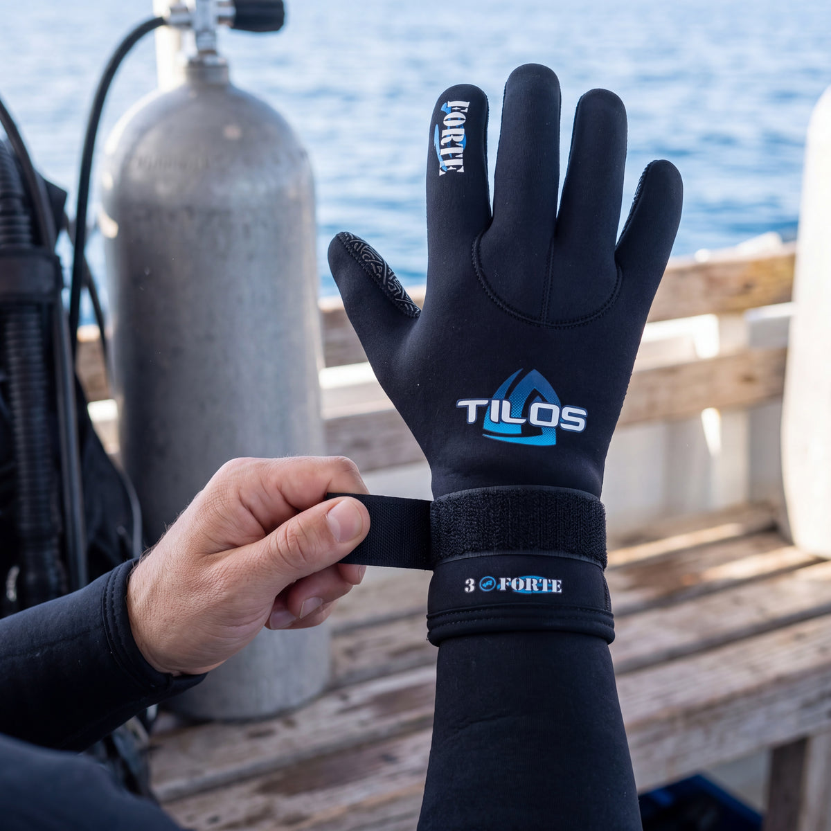 Diver on a dive boat bench wearing a black Tilos 3mm Forte Velcro Glove, pulling the velcro wrist strap snug before a dive