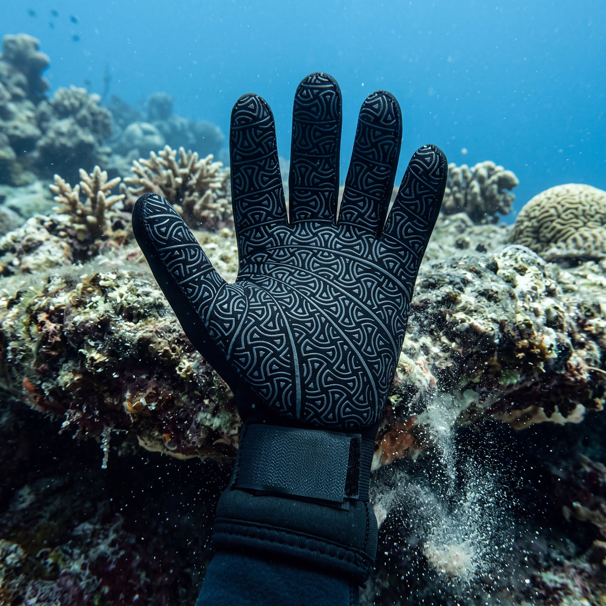 Diver underwater steadying a gloved hand on a rock ledge, showing the textured grip palm of a black Tilos 5mm Titanium neoprene dive glove.