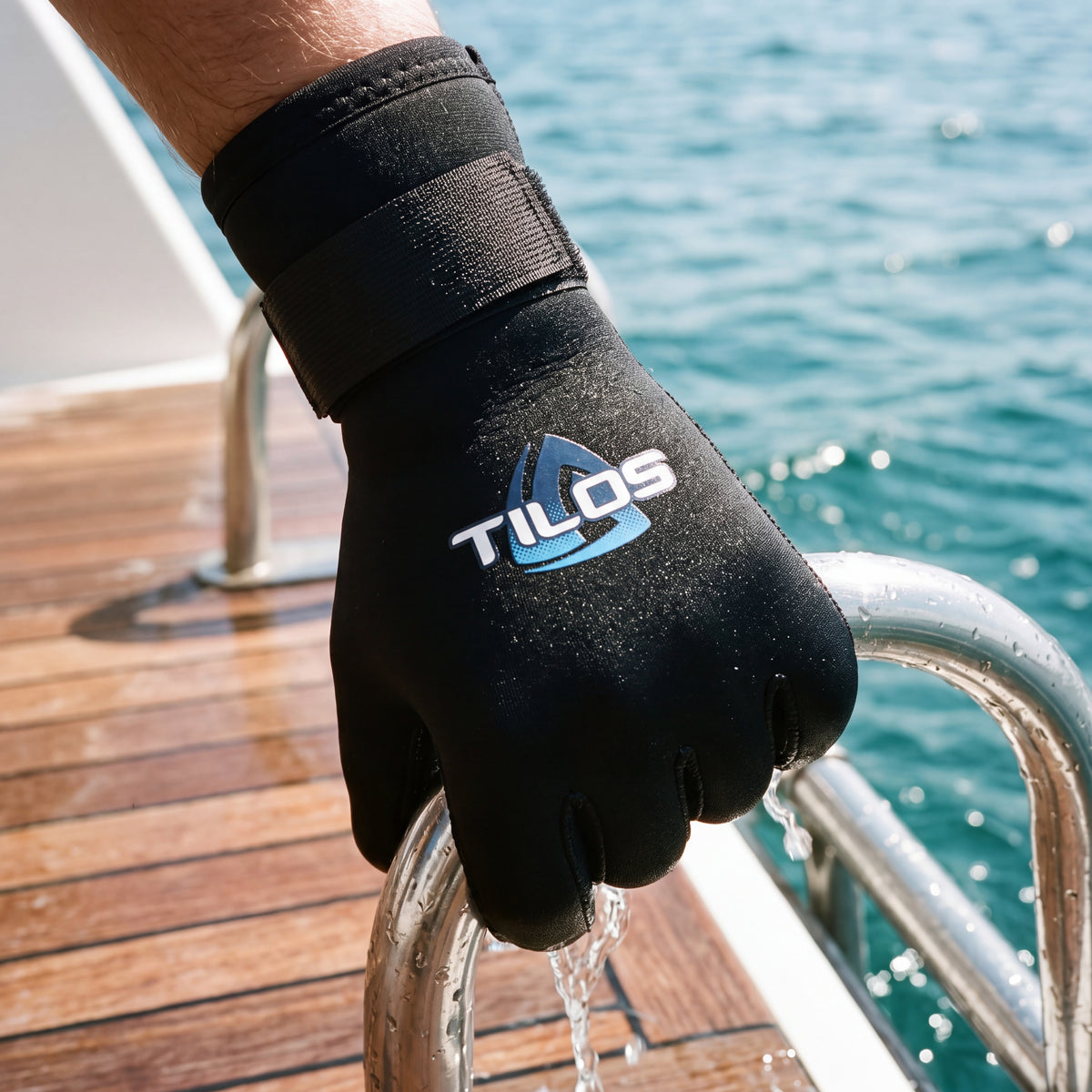 Diver gripping a dive boat ladder rail wearing a black Tilos 5mm Titanium neoprene glove, blue Tilos logo on the back of the hand.