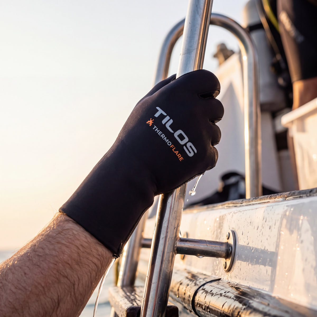Diver climbing out of the sea onto a dive boat ladder at golden hour, gripping the rail while wearing black Tilos 3mm Thermoflare dive gloves.