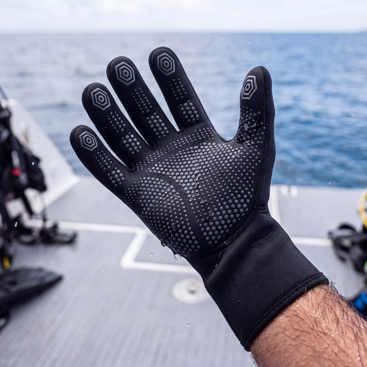 Close lifestyle detail of a diver on a boat deck turning a black Tilos 3mm Thermoflare dive glove palm up to show its silicone grip dots.