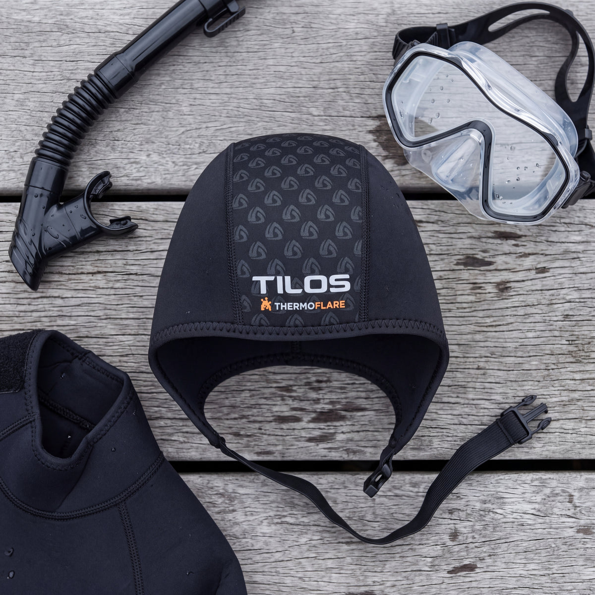 Top down lifestyle flat lay of the Tilos 1mm Thermoflare Chin Strap Beanie in black with mask and snorkel on a dock