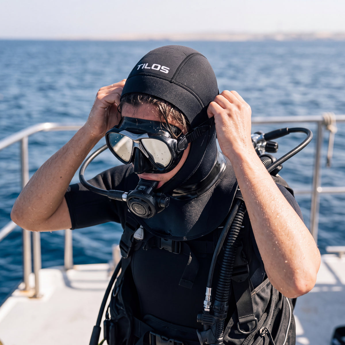 A diver pulling on a black Tilos 3mm neoprene dive hood on the deck of a dive boat before a dive.