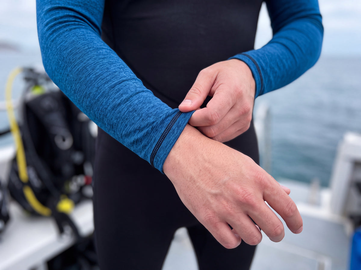 Close first person view of a diver pulling the sleeve cuff of the Tilos 6oz unisex skin suit down over the wrist while gearing up.