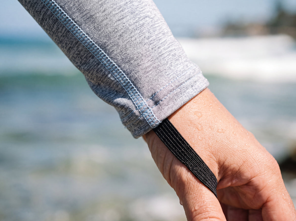 Close detail of a woman wearing the Tilos Women’s UPF 50+ Lycra Skin Suit, showing the black elastic thumb loop and light-blue flatlock stitching at the wrist cuff