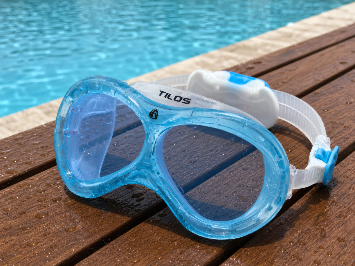Transparent Blue Tilos Dyno toddler swim mask on a wet wooden pool deck poolside after a swim