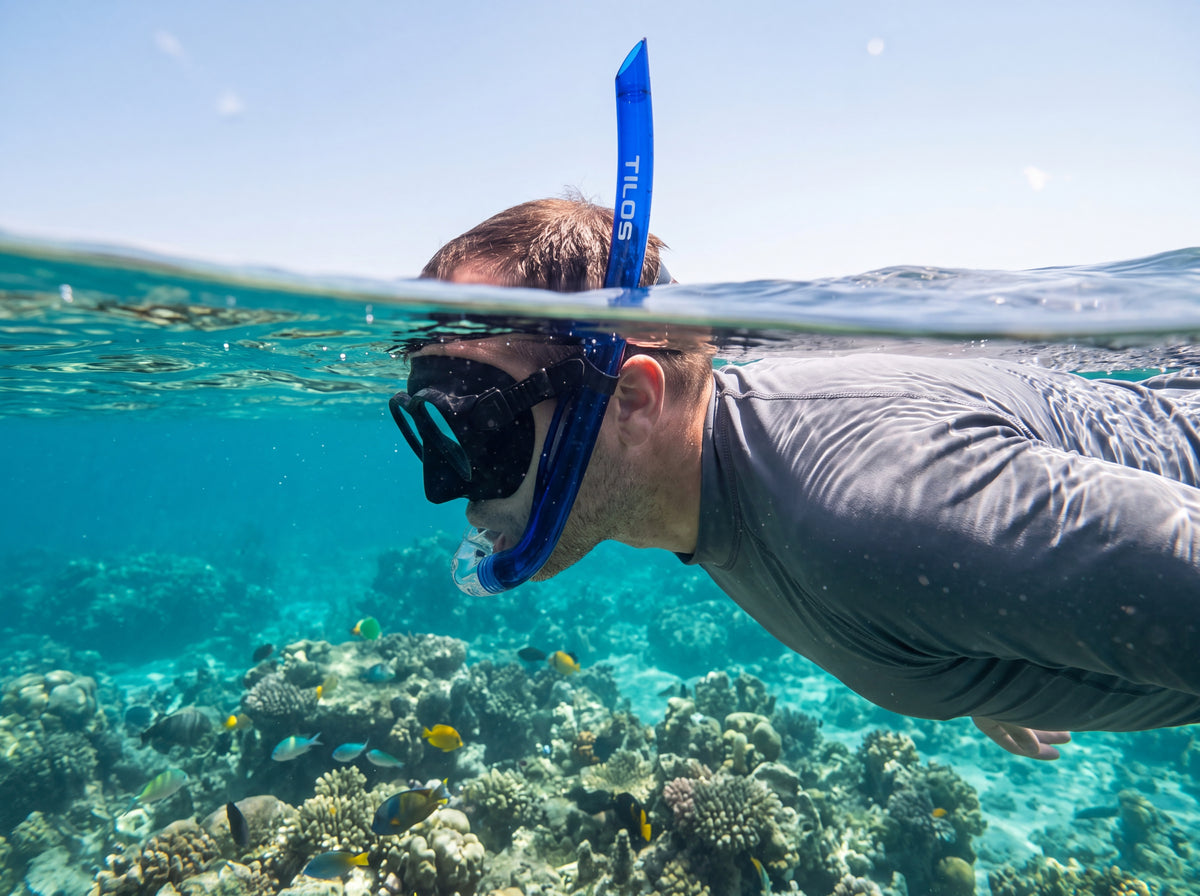 Snorkeler floating at the surface over a shallow coral reef breathing through the Tilos Basic J Snorkel in transparent blue