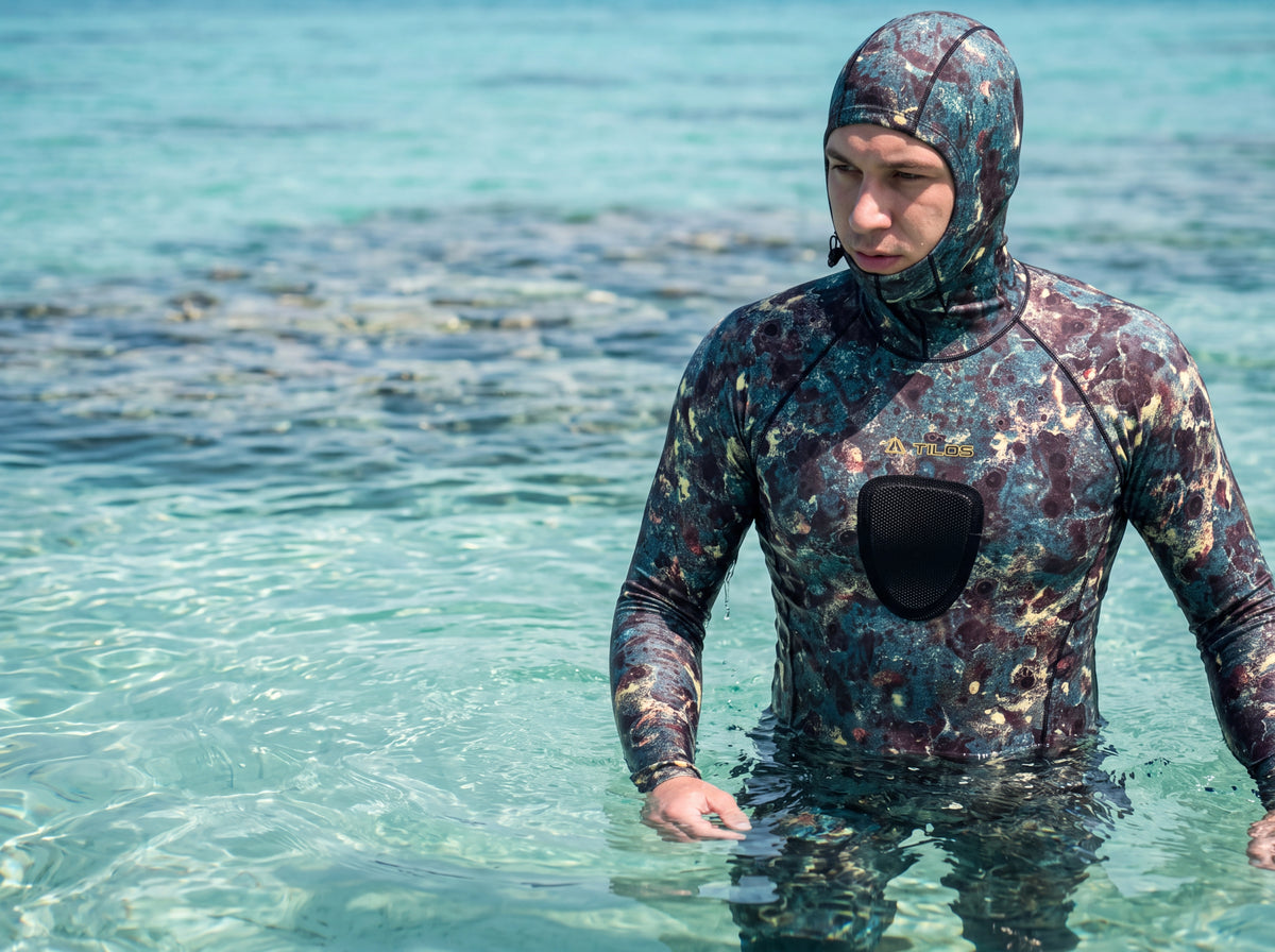 Freediver wearing the green camo Tilos hooded spearfishing shirt while standing in shallow open water