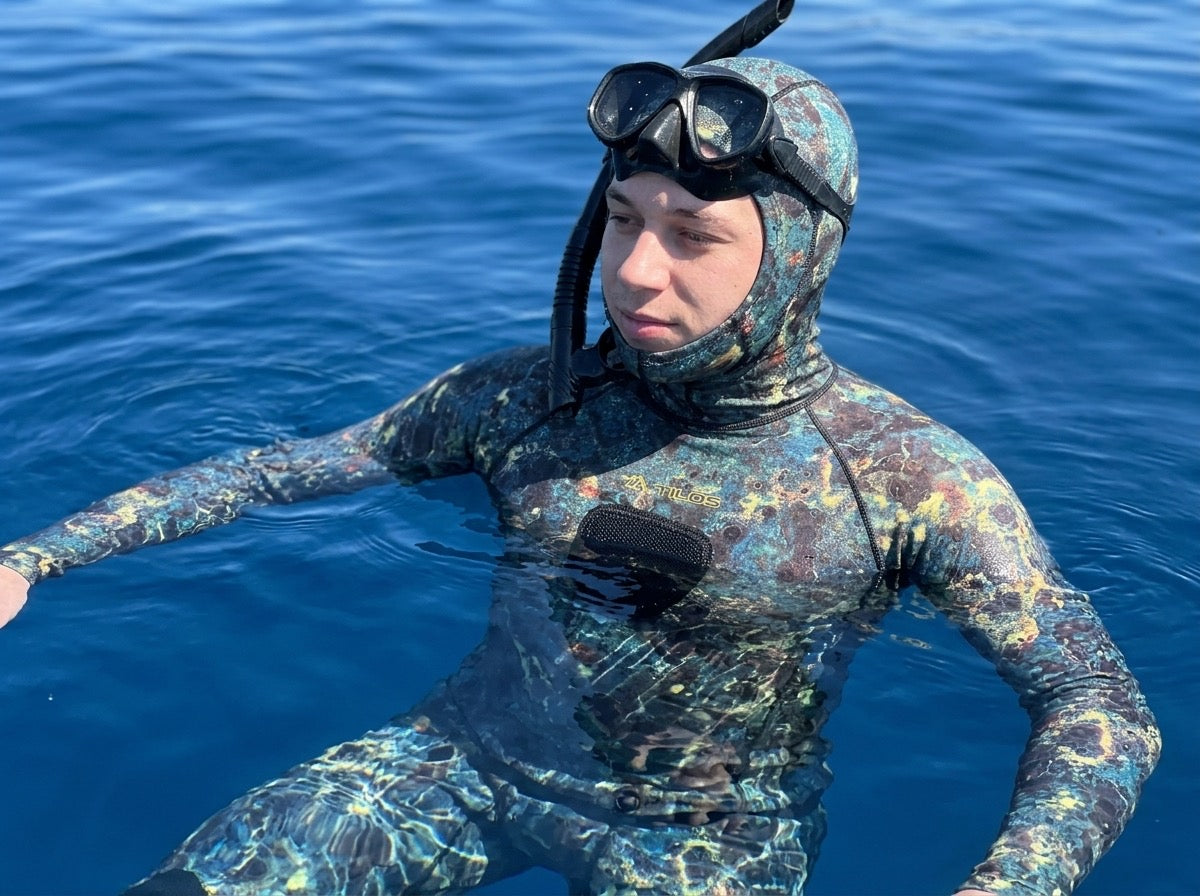 Freediver floating at the surface of deep blue water wearing the hooded Tilos Spearfishing Shirt in oceanic green camo