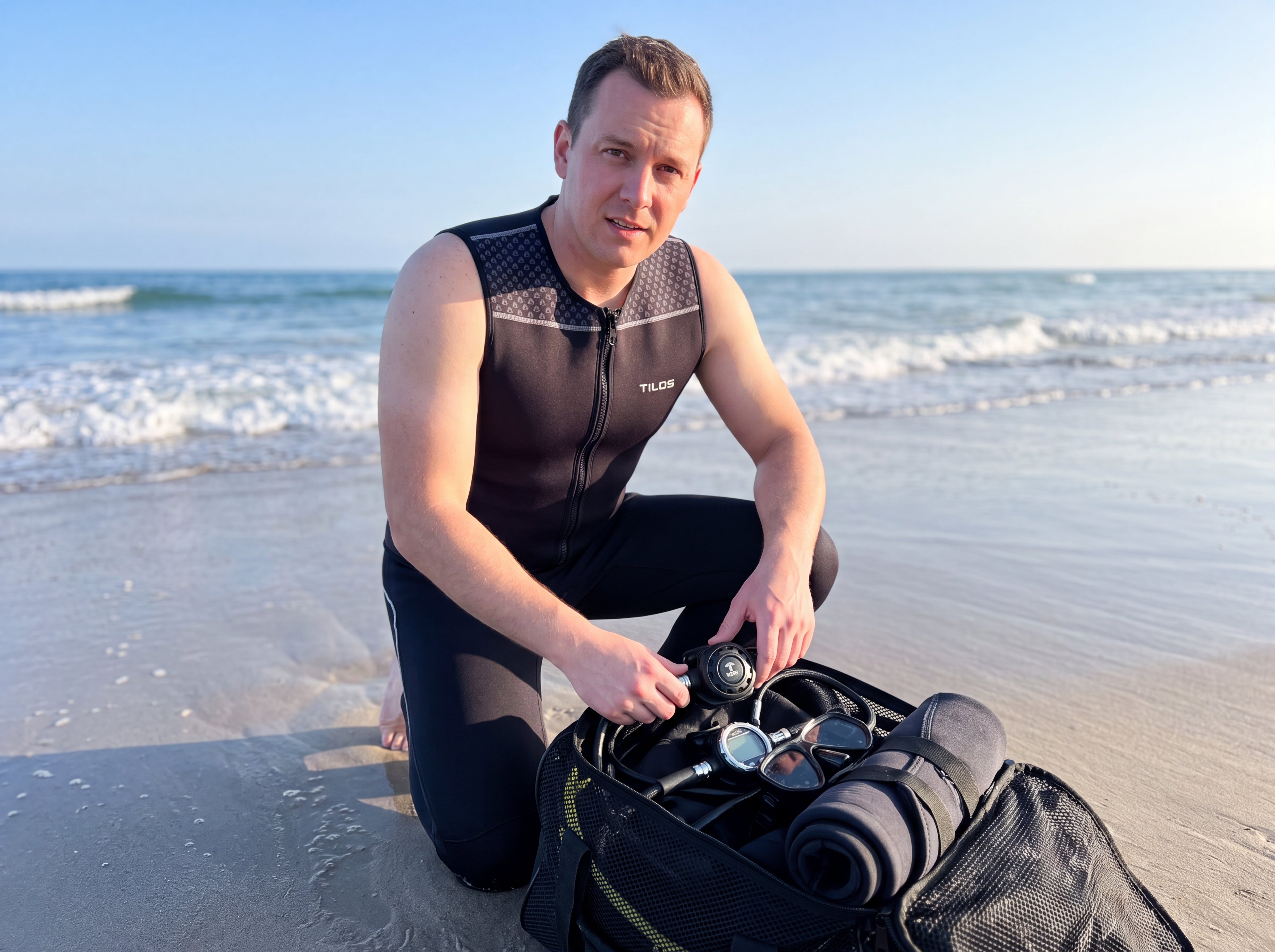 Diver kneeling on the beach with dive gear wearing the Tilos 1mm Mens Thermoflare Front Zip Vest